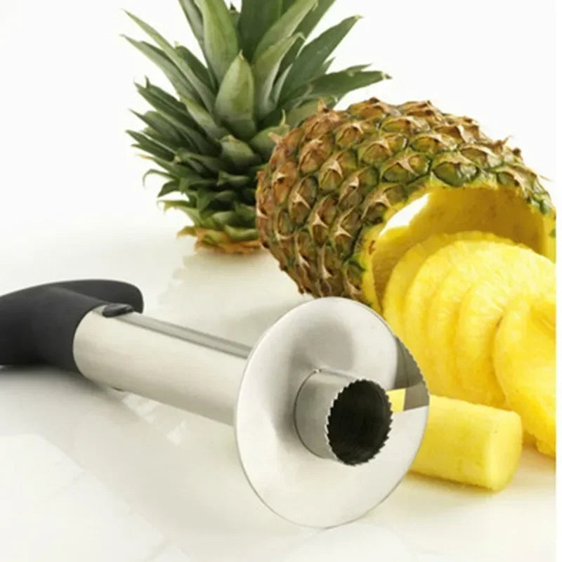 Corer lying on its side showing the serrated cutting ring, with a spiral-sliced pineapple behind