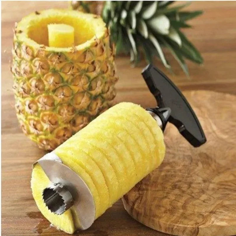 Stainless steel corer holding a spiral-cut pineapple cylinder beside the hollowed fruit on a wooden board